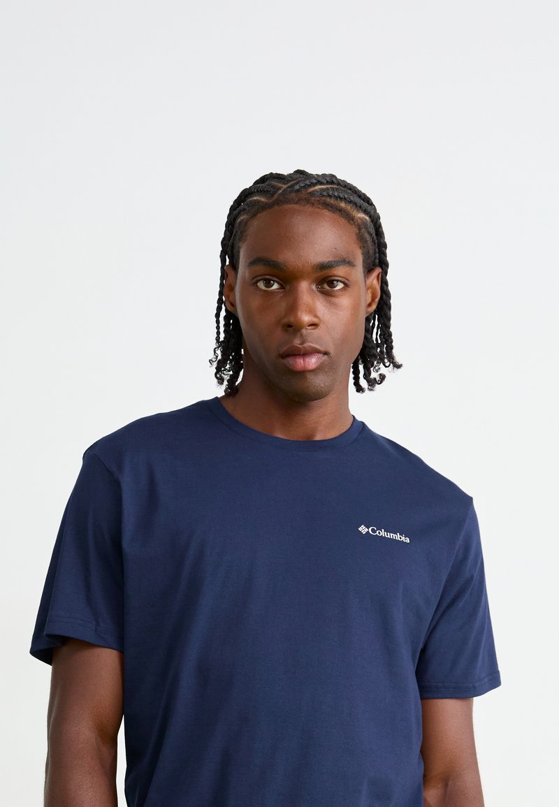 Navy blauwe katoenen t-shirt met korte mouwen, ronde hals en een klein wit Columbia-logo op de linkerkant van de borst. Glad van textuur.
