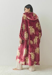 Red plush oversized robe with a hood, featuring a textured design of cream-colored fluffy animals. Long sleeves, relaxed fit, soft fabric.