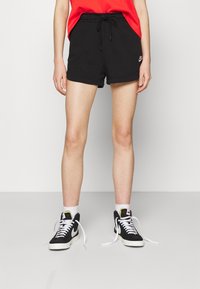 Black cotton shorts with an elastic waistband, featuring a drawstring and a small white Nike logo. Paired with black high-top sneakers.