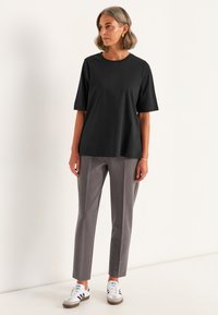 Musta lyhythihainen t-paita pyöreällä kaula-aukolla, yhdistettyinä harmaisiin muotovalaisimiin ja valkoisiin lenkkikengiin, joissa on mustia yksityiskohtia. Tasainen kangaslaatu.