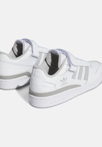 White leather sneakers with grey accents, featuring a padded collar, hook-and-loop strap, and three-stripe design on the sides.