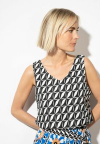 Ärmelloses Oberteil in Schwarz-weiß mit V-Ausschnitt, das geometrische Formen zeigt. Weiches Material, lockere Passform, kombiniert mit einem gemusterten Rock.