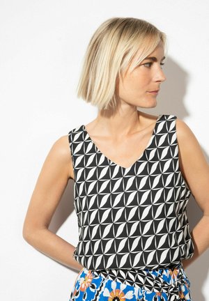 Ärmelloses Oberteil in Schwarz-weiß mit V-Ausschnitt, das geometrische Formen zeigt. Weiches Material, lockere Passform, kombiniert mit einem gemusterten Rock.