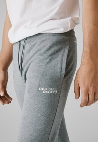 Sivé tepláky s jemnou textúrou, s nastaviteľným pásom na šnúrku a bielym logom "RED BULL RACING" na ľavom stehne.