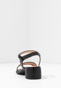 Mustan nahkaisen korkokenkäsandaalin rounded toe ja nilkkahihna. Siinä on matala lohkare, ja sisävuori on sileä.