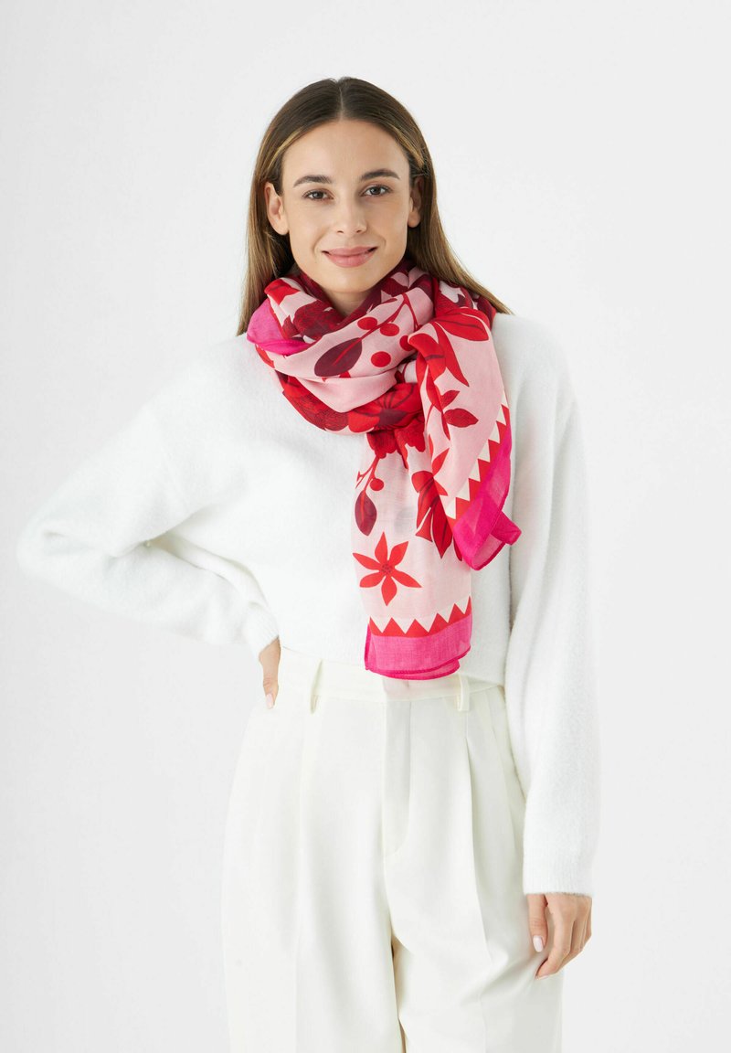 Écharpe multicolore présentant un motif floral dans des nuances de rose et de rouge, avec un design de bord triangulaire, drapée autour du cou du modèle.