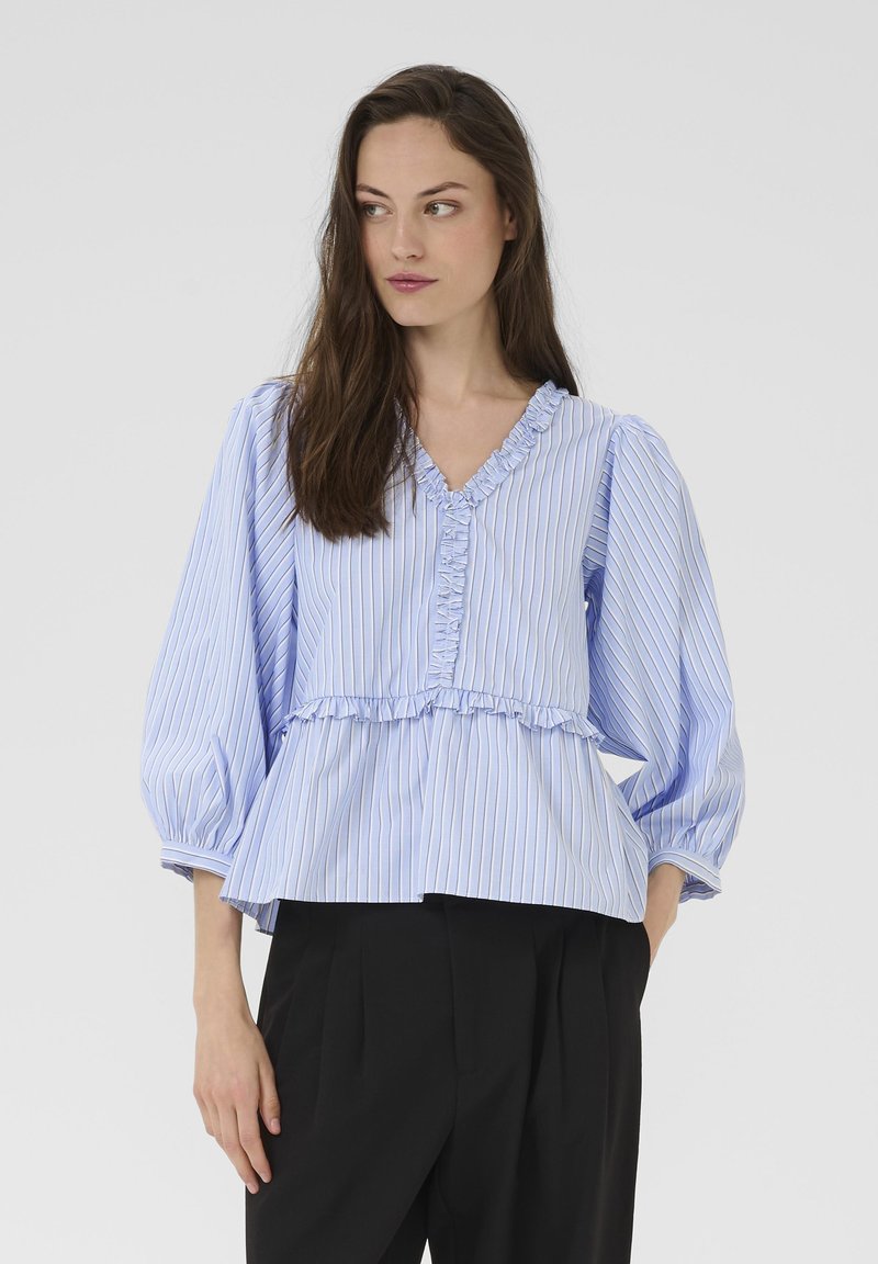 Bluza dungi albastru deschis cu decolteu cu volane și design în straturi. Are mâneci lungi, bufante și croială lejeră. Asortată cu pantaloni negri.