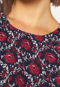 Tejido azul marino con un patrón floral que presenta flores rojas y blancas. Cuello redondo, textura suave y acentos de bordado detallado.