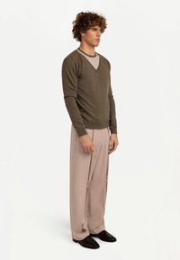 Olivgrön tröja med V-ringning, kombinerad med ljusbeiga plisserade byxor. Svarta skor fulländar outfiten. Mjuk textur överlag.