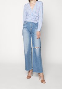 Top avvolgente a strisce blu con maniche lunghe, abbinato a jeans a gamba larga di un azzurro chiaro a vita alta con dettagli strappati sulle ginocchia.