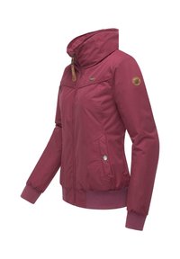Veste bordeaux avec un col haut, fermeture éclair à l'avant et poignets élastiques. Dispose de poches latérales et d'un détail de badge sur la manche. Texture de tissu lisse.