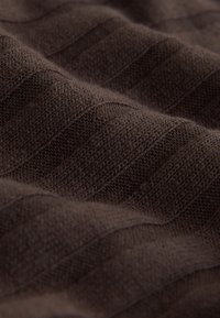 Tissu tricoté marron avec un motif texturé présentant des lignes diagonales en relief, offrant une surface douce et lisse.