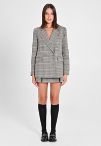 Blazer doppiopetto a quadri grigio e nero, abbinato a una gonna coordinata, calze nere al ginocchio e mocassini neri lucidi.