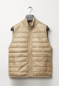 Beige pehmeä, vuorattu, hihaton puffaliivi, jossa on vetoketjukiinnitys ja ribbikuvioitu kaulus, roikkumassa harmaalla ripustimella valkoista taustaa vasten.