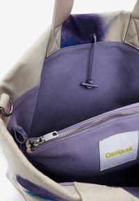 Borsa in tela con una tasca interna con zip. Motivo a schizzi colorati sul bordo, rivestimento lavanda e un'etichetta con il marchio "Desigual."