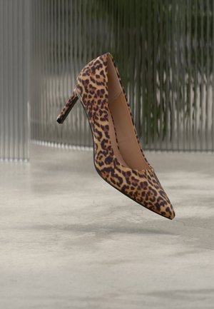 Γόβα με τακούνι και λεοπάρ σχέδιο, μυτερή μύτη, αιωρείται πάνω από γυαλισμένο κονιαμένο πάτωμα με φόντο ραβδωτό γυαλί.