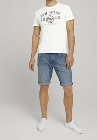 Camiseta blanca con estampado gráfico rojo, pantalones cortos de mezclilla en azul claro, con los puños doblados, y zapatillas blancas. Conjunto de verano simple y casual.