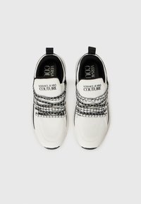 Hvite atletiske sko med en teksturert mesh-overdel, svarte detaljer og karakteristiske svart-hvite mønstrete snørebånd med logodetaljer.