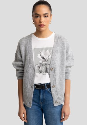 Gray knitted cardigan with a deep V-neck, large buttons, and ribbed cuffs worn over a white graphic T-shirt and blue jeans.