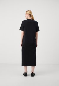 Black, knee-length dress with short sleeves, featuring a simple, straight design and a smooth texture. Worn with black shoes.