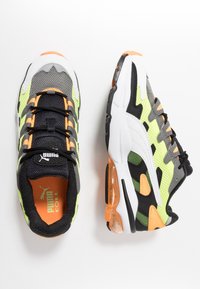 Puma-sneakers med övre i mesh och textil. Färger inkluderar svart, grått, gul-grön och orange detaljer. Har en vadderad sula.