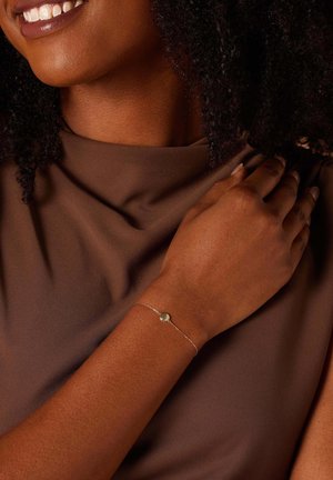 Zilveren schakelarmband met een ronde hanger. De hand heeft een natuurlijke huidtoon en ligt op een bruine stoffen achtergrond.