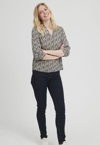 Bloemmotief blouse in donkere tinten met 3/4 mouwen en een relaxed fit, gecombineerd met marineblauwe skinny jeans en witte sneakers.