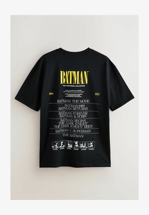 Zwarte T-shirt met korte mouwen, featuring witte tekst met een opsomming van Batman-films van 1966 tot 2022, met bovenaan een groot geel "BATMAN"-logo.