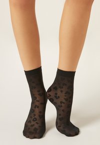 Černé průhledné ponožky s leopardím vzorem, s jednobarevným černým lemem nahoře. Hladká textura a délka po kotníky.