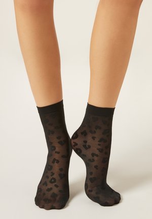 Svarta genomskinliga strumpor med leopardmönster och en solid svart mudd högst upp. Mjukt material och ankellängd.