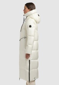 Lang dynejakke i skinnende hvid med hætte, lynlåslommer og sorte detaljer. Quiltet design med lige snit, midi-længde.