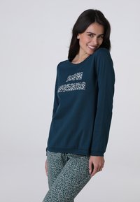 Maglietta a maniche lunghe di colore teal con la scritta "SLOW MORNING" in un design a stampa, abbinata a pantaloni a stampa leopardata verde. Tessuto morbido, vestibilità casual.