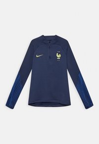 Tummansininen pitkähihainen urheilupaita, jossa on neljännesvetoketju, keltainen Nike-logo, Ranskan jalkapallojoukkueen emblem sekä kuviollinen kangas alaosassa hihoissa.