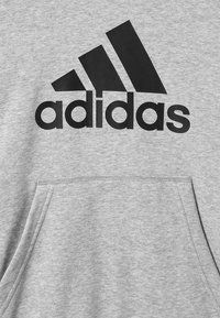 Sudadera con capucha gris hecha de mezcla de algodón, con un gran logo negro de “adidas” y un bolsillo tipo canguro en la parte delantera. Textura suave, diseño clásico.