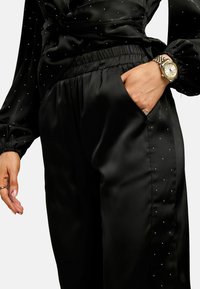 Melni satīna bikses ar elastīgu jostasvietu, sānu kabatu un smalku punktētu rakstu. Gluda tekstūra, pieguļoša piegrieztne un relaksēta siluets.