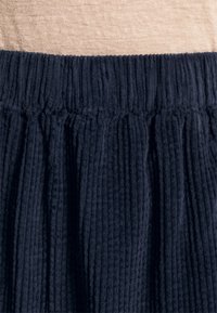 Tumedate triibuline kangas, millel on sooneline tekstuur ja elastne vöökoht. Tekstiilil on pehme, karvane välimus.