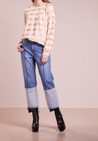 Felpa rosa con stampe animali dorate, abbinata a jeans di denim blu con design a patchwork e stivali neri con zeppa.