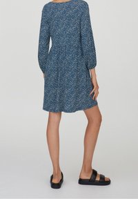 Robe à imprimé floral bleu marine avec manches trois-quarts, taille froncée et coupe ample. Associée à des sandales plates noires.