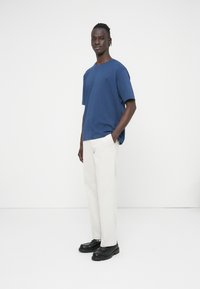 Μπλε κοντομάνικο μπλούζα με στρογγυλή λαιμόκοψη, συνδυασμένη με ανοιχτό μπεζ παντελόνια και μαύρα παπούτσια. Απλός σχεδιασμός, απαλή υφή και άνετη εφαρμογή.