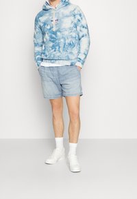 Light blue tie-dye hoodie with drawstring, paired with light denim shorts. White sneakers and ankle-length socks complete the look.