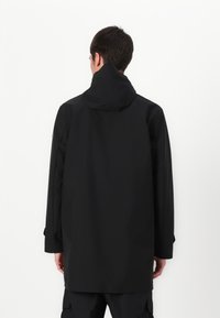 Zwarte regenjas met een capuchon, voorzien van een gladde, matte afwerking, lange mouwen en een comfortabele pasvorm, gezien van achteren.