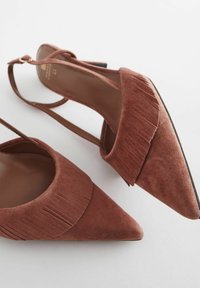 Smeđi nubuk slingback potpetice s šiljastim prstima, s frufrusima duž pjenastog ovratnika i tankim remenom oko gležnja s zlatnom kopčom.