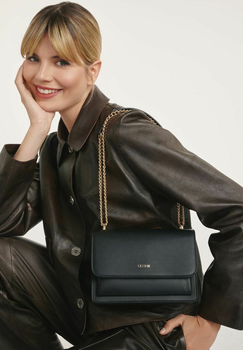 Czarna skórzana torebka na ramię z złotym łańcuchem, o strukturalnym designie i z przodem na klapkę. Gładka faktura i minimalistyczne detale.
