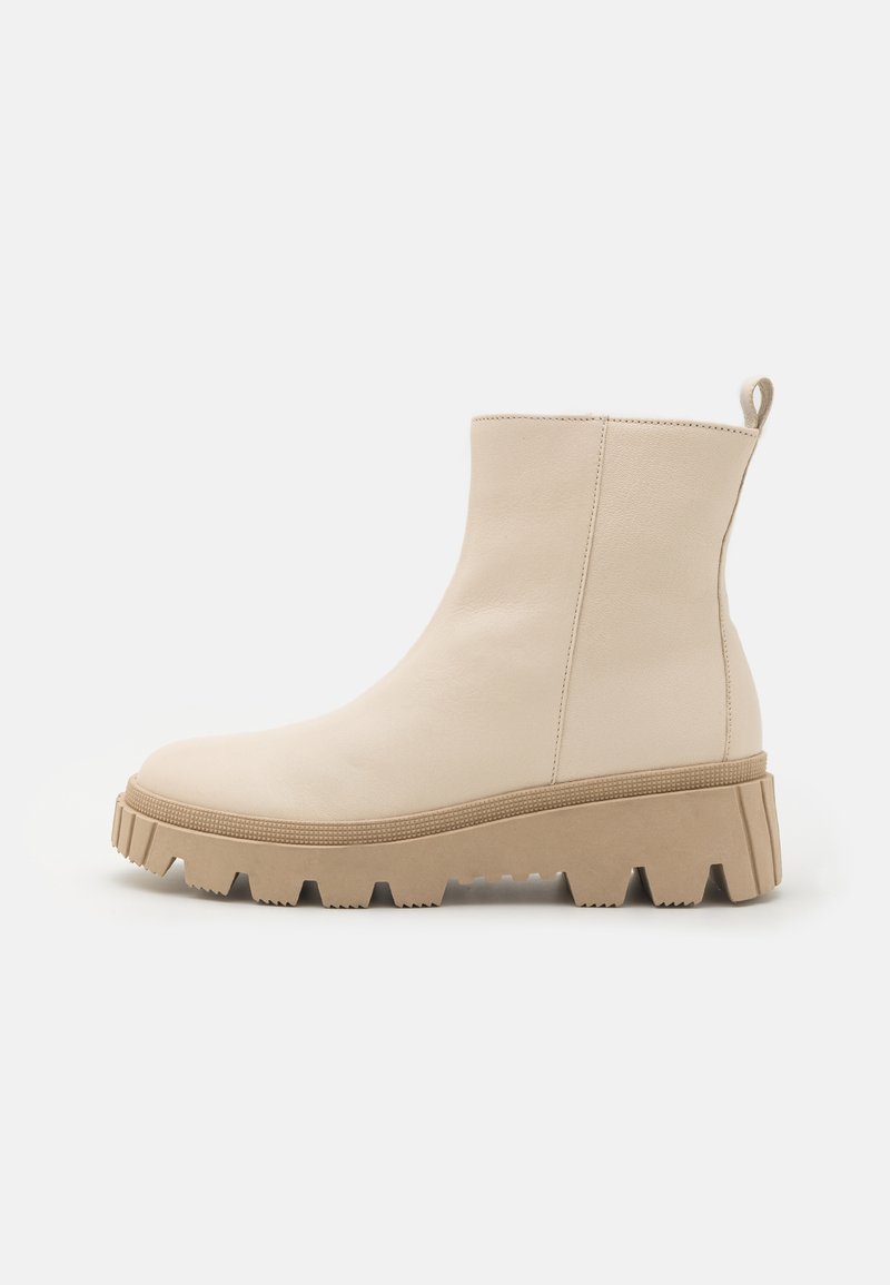 Bottines beiges avec une finition en cuir lisse, dotées d'une semelle en caoutchouc texturée et épaisse, et d'unentab pour un enfilage facile à l'arrière.