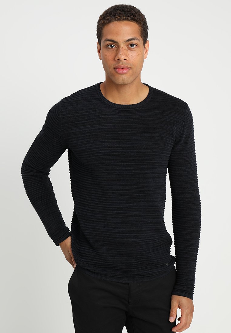 Maglione nero a coste con maniche lunghe e colletto a girocollo. Caratterizzato da un tessuto testurizzato e una silhouette aderente, abbinato a pantaloni scuri.