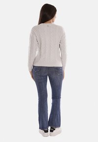 Maglione grigio chiaro a maglia con orlo a coste, indossato con jeans a zampa d'elefante blu scuro e sneakers bianche con dettagli neri. Vista posteriore.