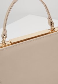 Beżowa skórzana torebka o gładkiej fakturze, z wyraźnym kształtem, złotymi elementami i krótkim uchwytem. Zapięcie z eleganckim metalowym zapięciem.