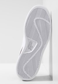 Suela de zapato deportivo blanco con un patrón texturizado en zigzag, que presenta el logo de Puma en la sección interior, montada verticalmente contra un fondo neutro.