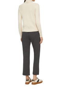 Pull en maille crème à col roulé associé à un pantalon de jogging gris foncé et des baskets blanches avec des accents dorés. Texture lisse, design ajusté.
