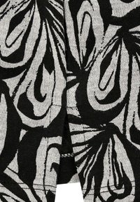 Schwarz-weiß gemusteter Stoff mit großen, abstrakten botanischen Formen auf einem strukturierten Hintergrund, mit sichtbaren Faden-Details und Naht.